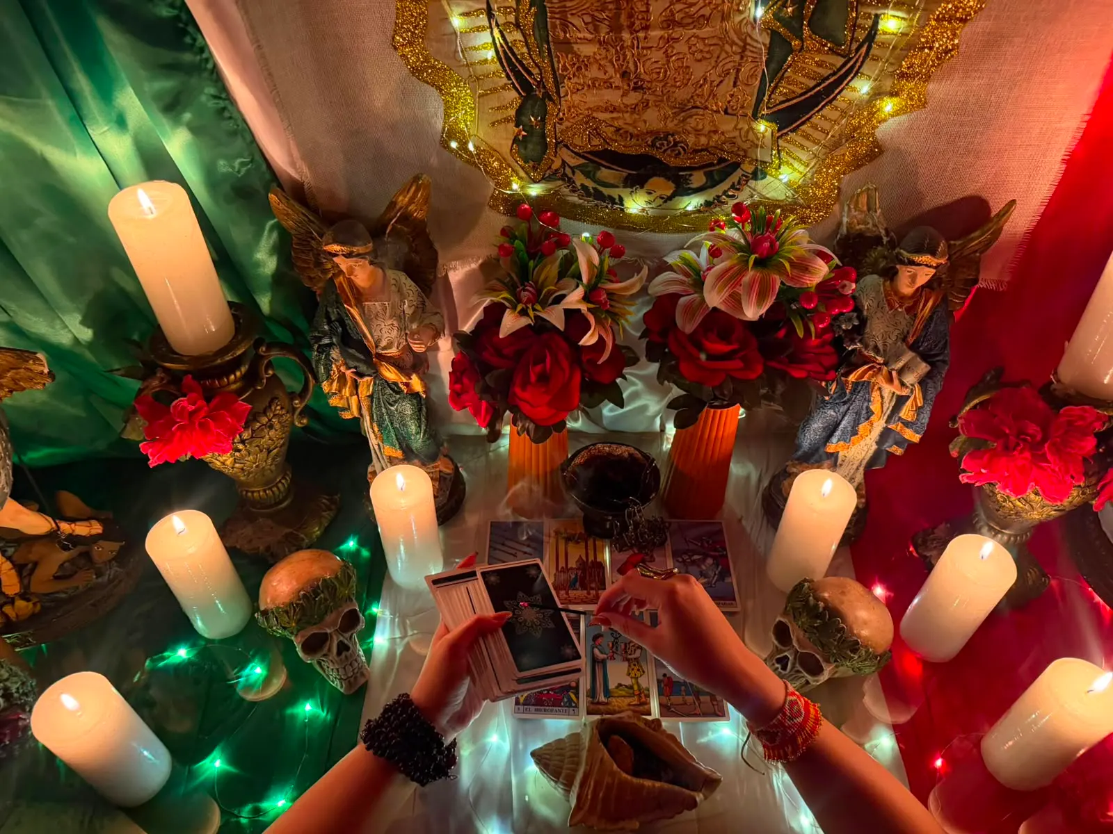 Tirada de cartas sobre el altar, entre velas blancas, flores rojas y figuras de ángeles