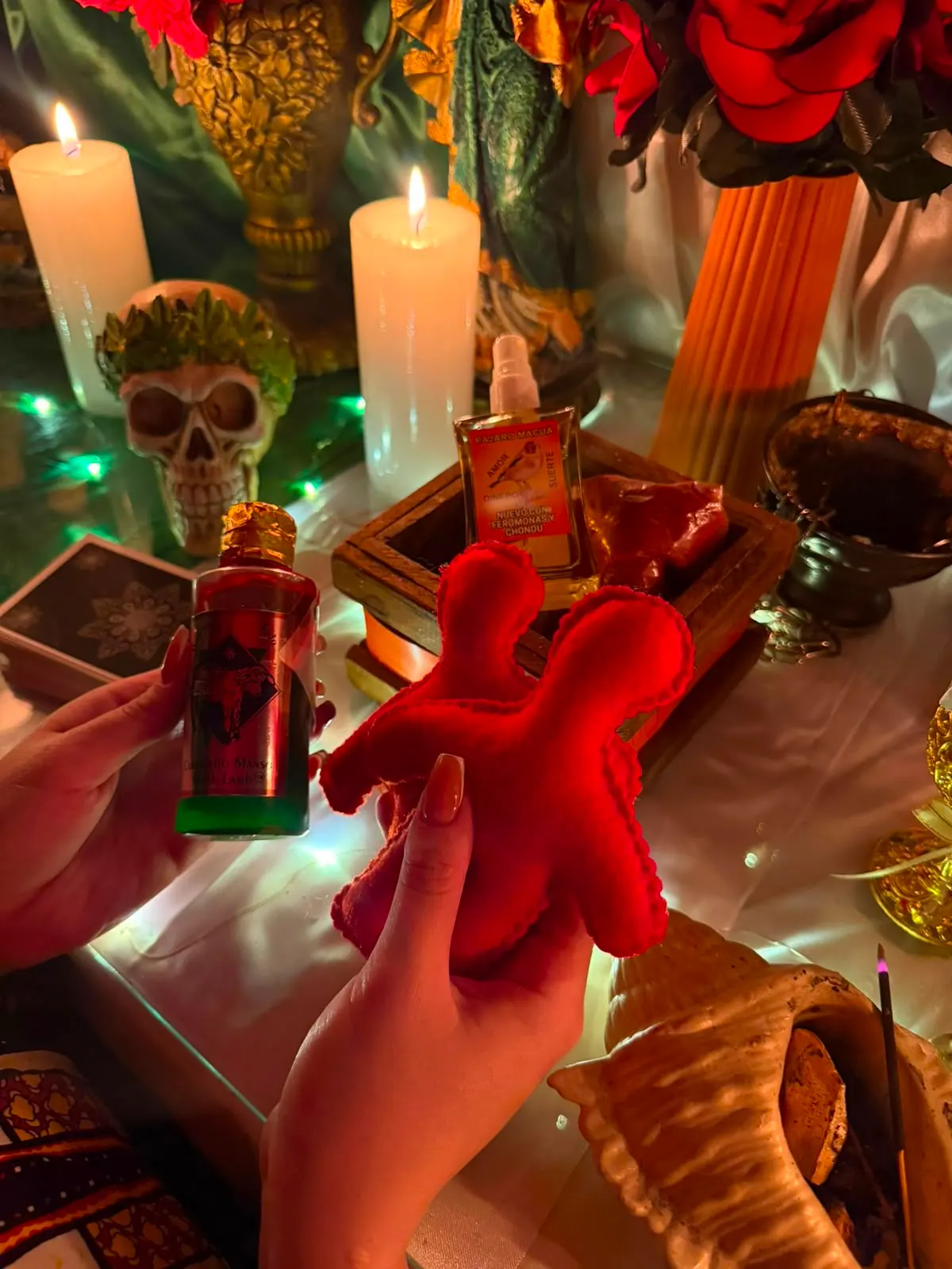 Figura de tela roja sostenida frente al altar, con velas encendidas y un frasco de esencia