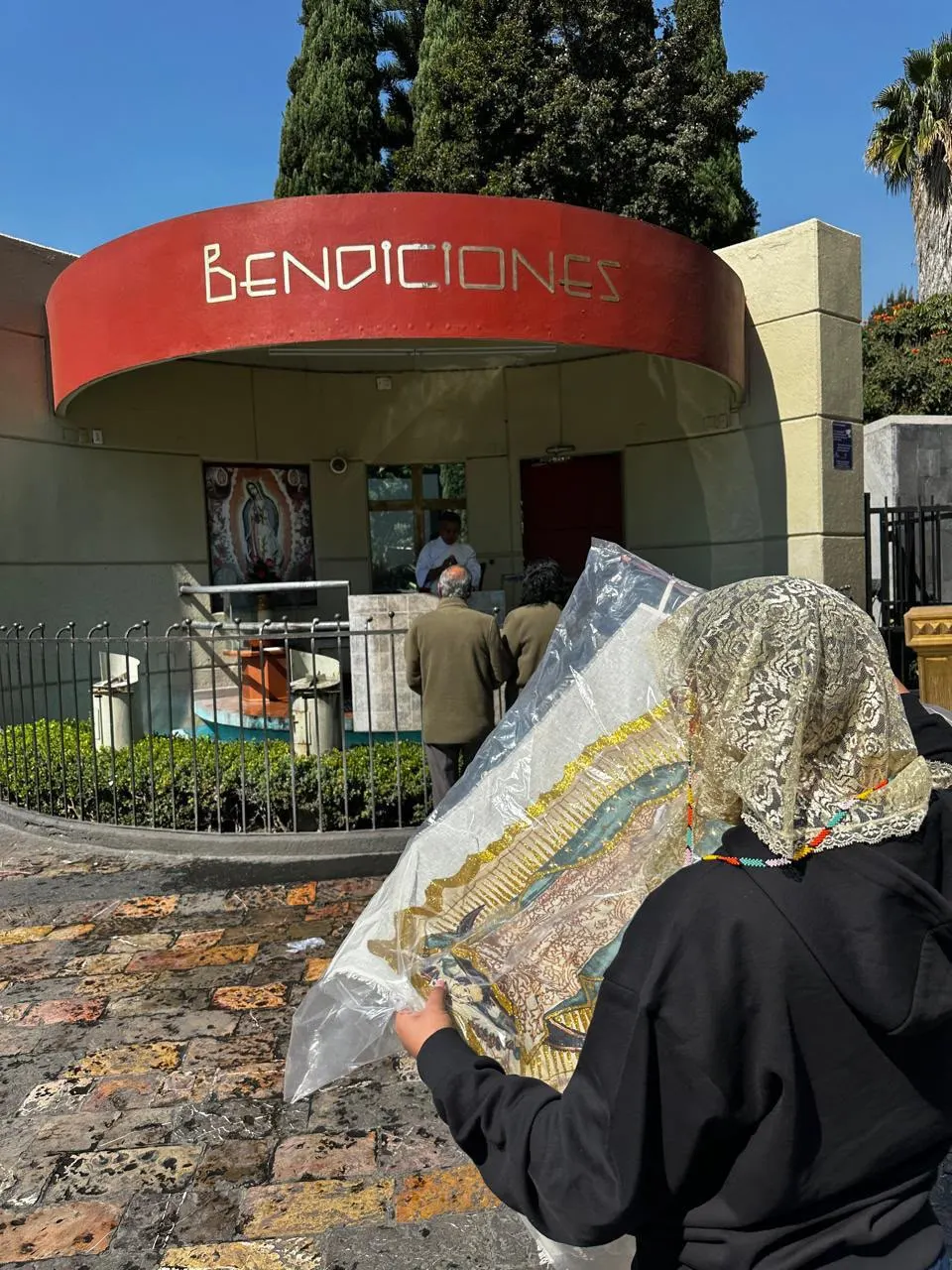 Persona con velo de encaje llevando una imagen de la Virgen de Guadalupe a bendecir a la iglesia