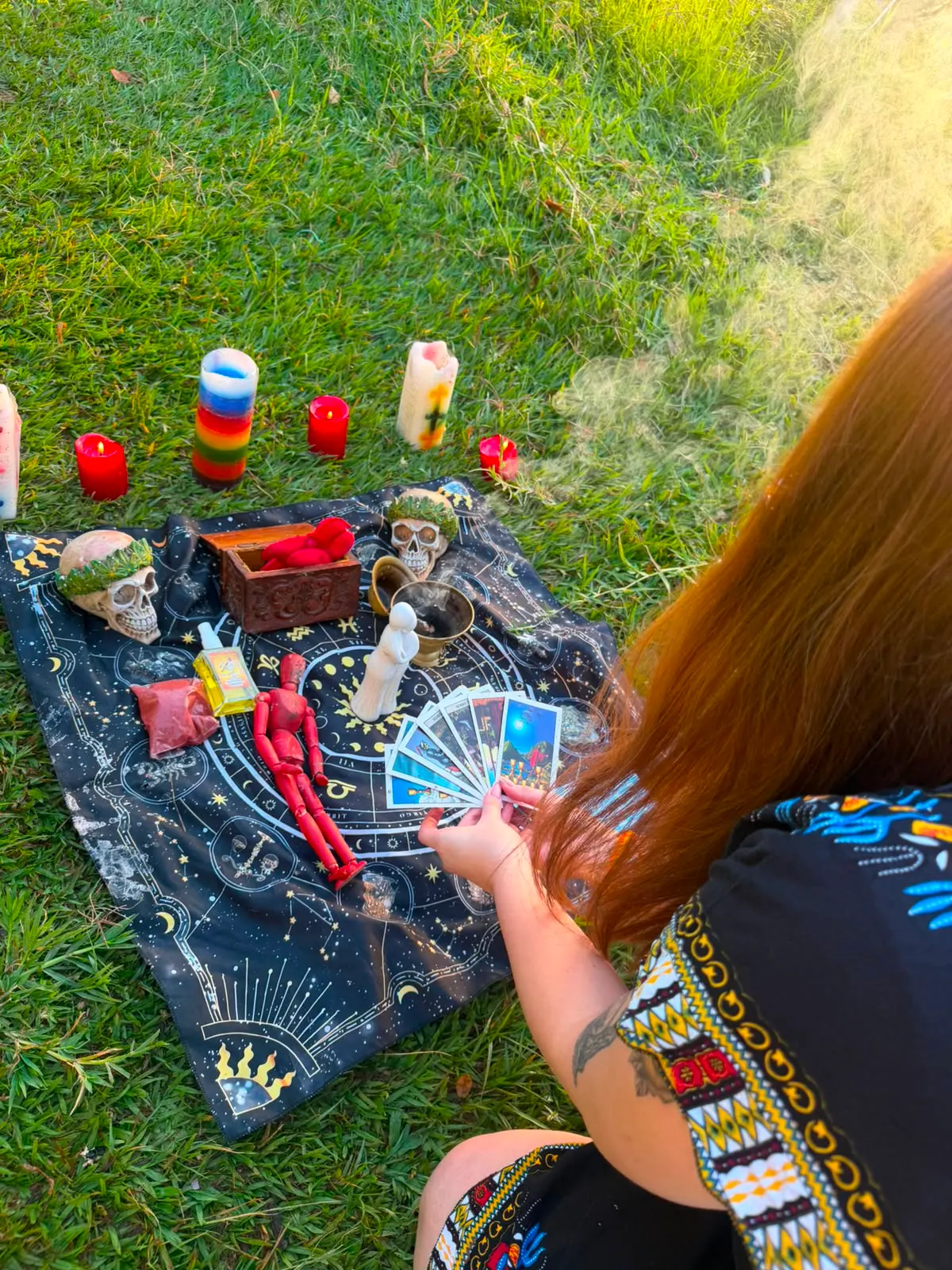 Ofrenda de apertura de camino al atardecer, sobre el pasto, con velas de colores y cartas