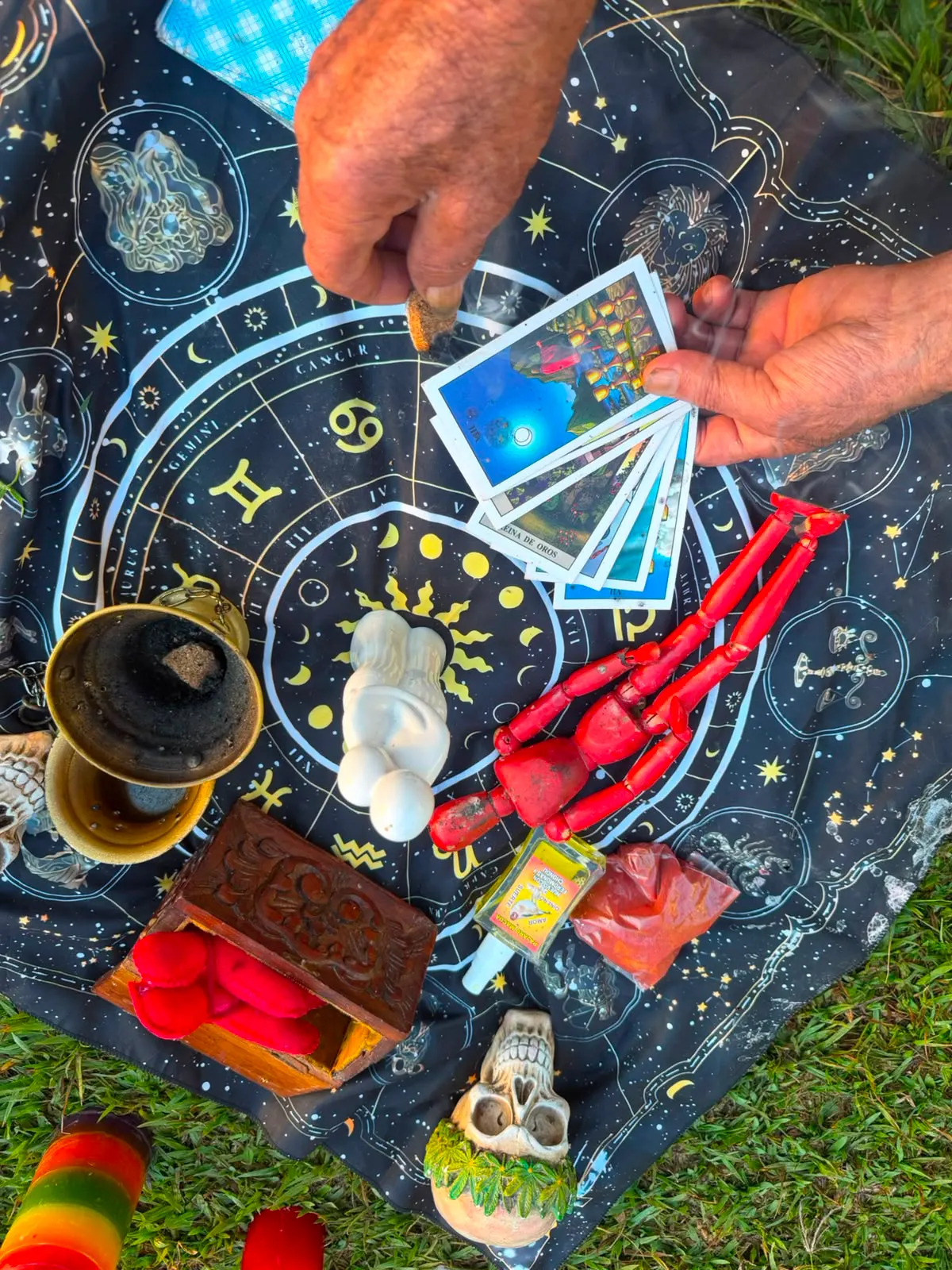 Manos de un maestro mostrando cartas del tarot sobre una ofrenda con dos figuras, velas y sahumerio