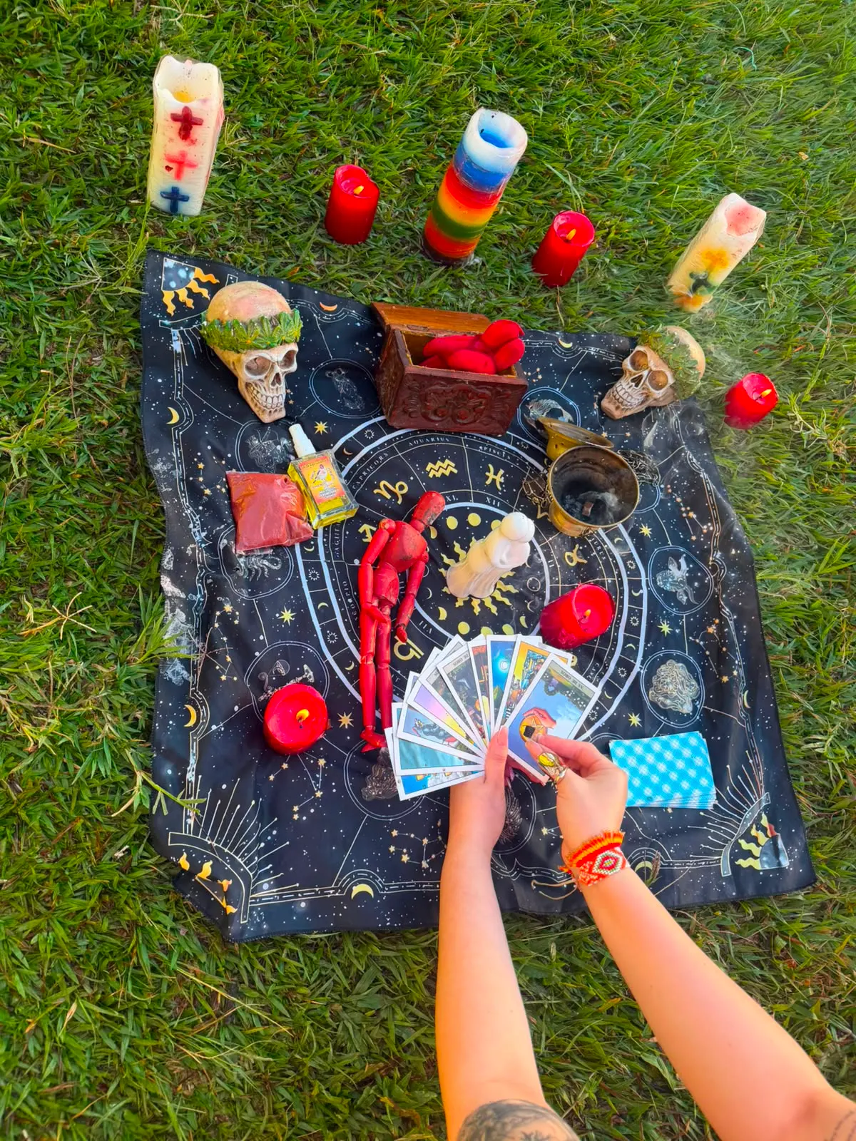 Ofrenda vista desde arriba: paño de estrellas, calaveras, velas rojas, una figura roja y cartas del tarot