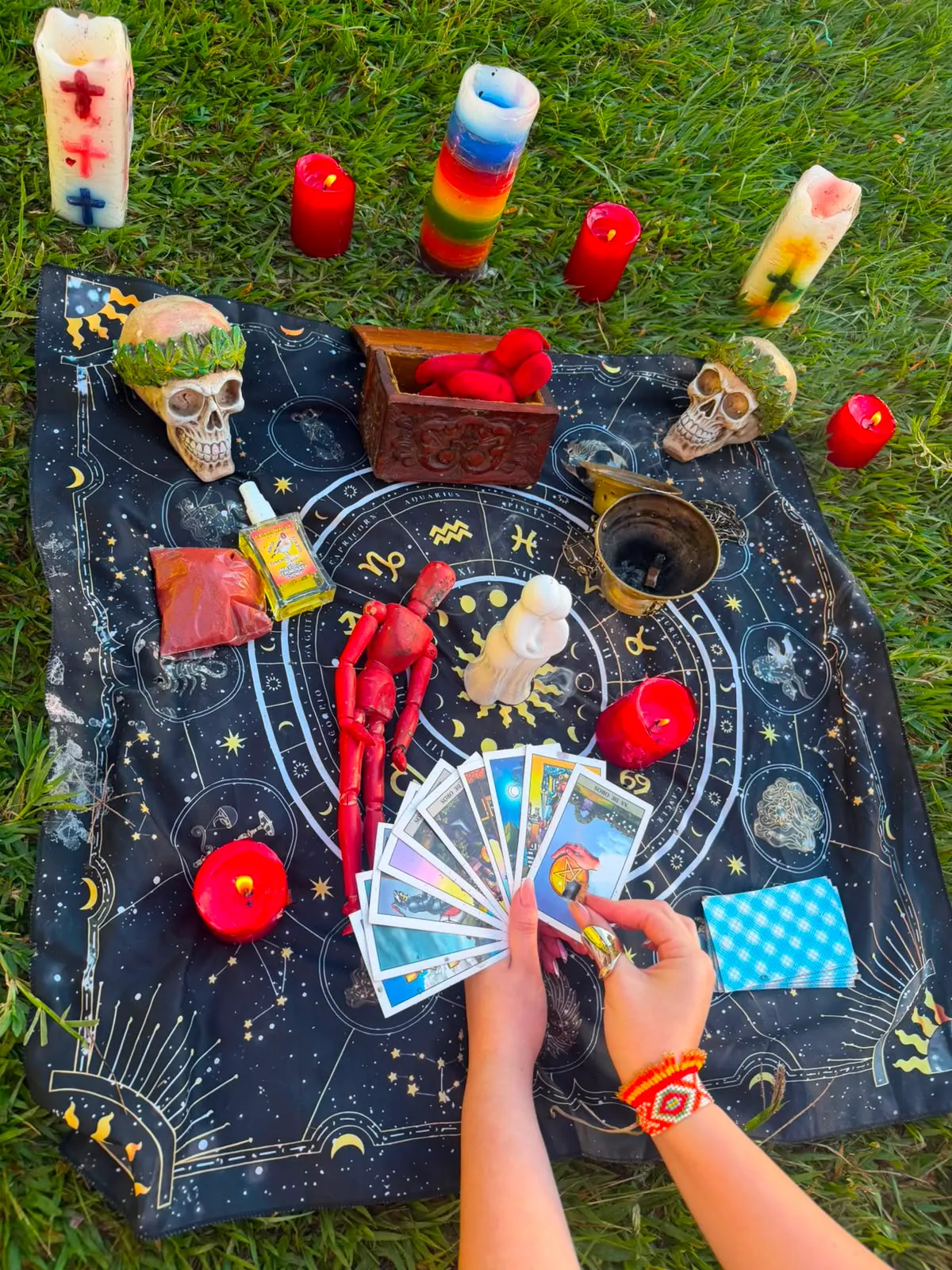 Ofrenda al aire libre sobre un paño de estrellas, con velas rojas, una vela de siete colores y cartas en abanico