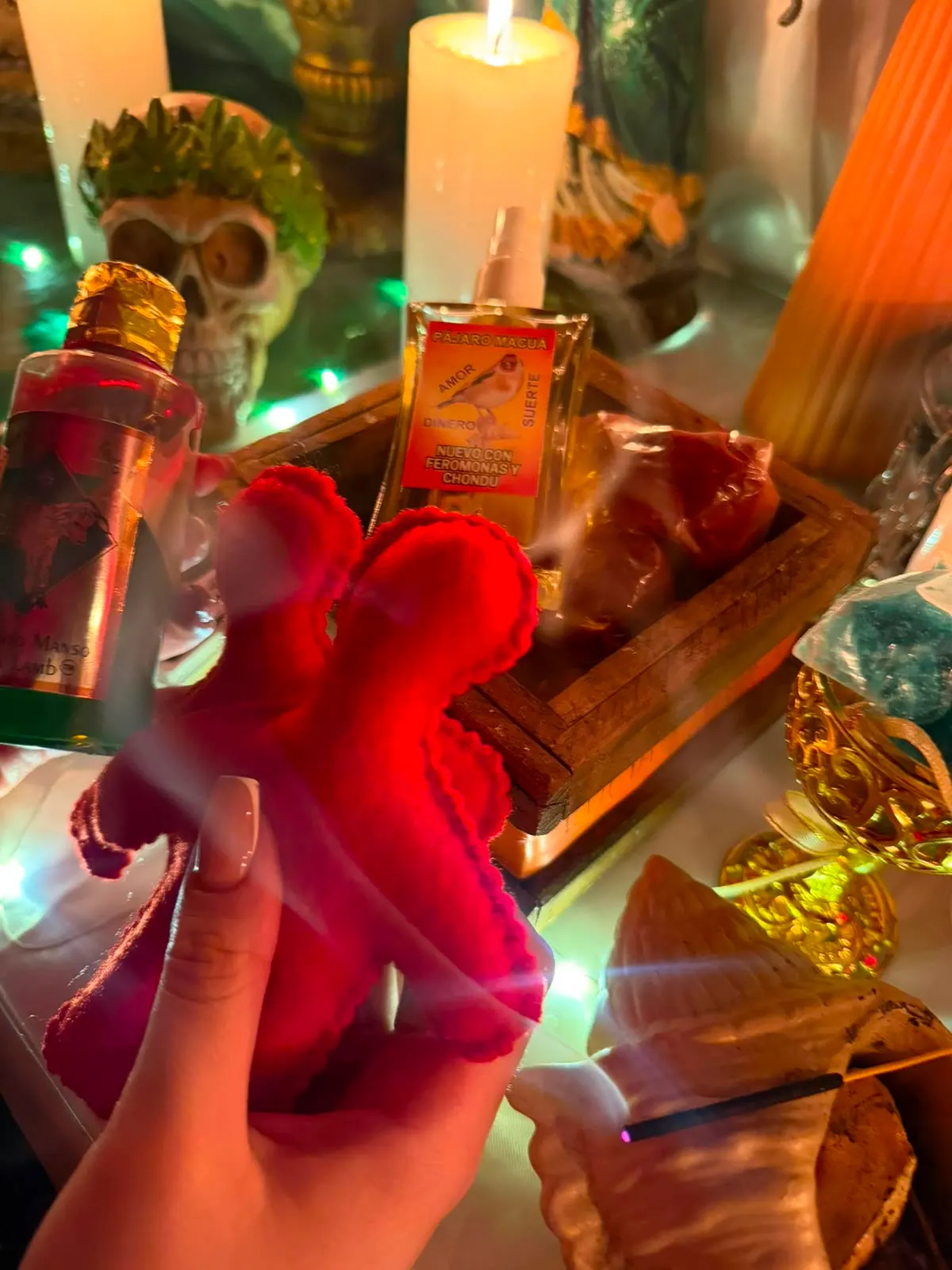 Figura roja de tela junto a una vela encendida, esencias y una caja de madera en el altar